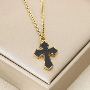 Détail d'un pendentif croix dorée avec centre en onyx noir et bordure perlée sur chaîne