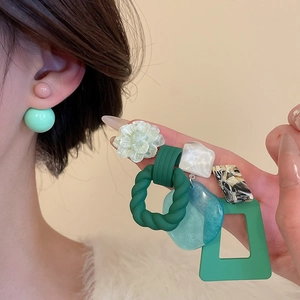 Detailed view of mint green acrylic studs and geometric resin drop earrings on a model