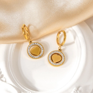 Détail de boucles d'oreilles cœur dorées avec cristaux blancs sur plateau vintage blanc