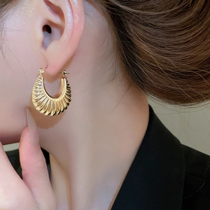 Detail of gold C-shaped hoop earrings with a textured corrugated finish on a model