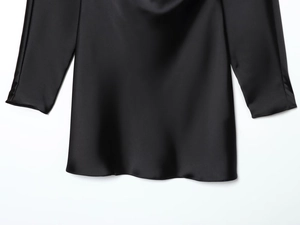 Détail de la robe en satin noir montrant la texture de soie sur l'ourlet et les poignets