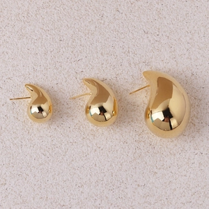 Three sizes of polished gold teardrop earrings displayed on a beige textured surface