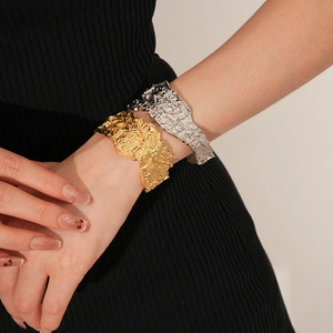 Dettaglio dei bracciali metallici a pieghe irregolari in oro e argento indossati da modella