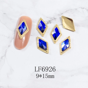 Detalle de dijes para uñas romboidales de 9x15mm con gemas azules y marco de metal dorado