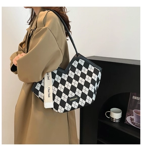 Model wearing a large checkerboard tote bag with lettered shoulder strap and coat