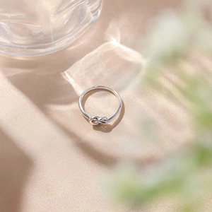 Close-up of a silver knot ring on warm beige silk background under natural sunlight