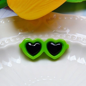 Macro shot of a small green resin heart sunglasses accessory for dolls on a ceramic plate