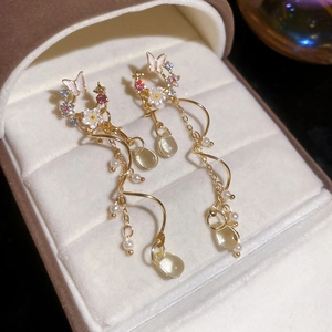 Detailed close-up of golden tassel earrings with white butterfly and acrylic floral accents
