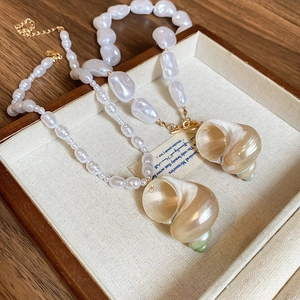 Detail of baroque pearl necklaces with natural conch shell pendants on a wooden tray
