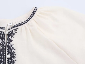 Close-up detail of black floral embroidery on a white women blouse collar with size S tag
