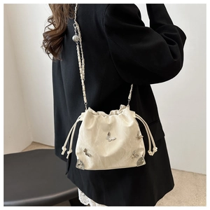 Detail of cream bucket bag with silver butterfly charm and woven chain strap on black blazer