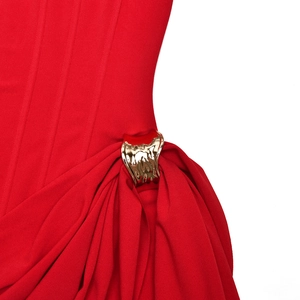 Detail of red pleated fabric with irregular golden fluid metal buckle ornament