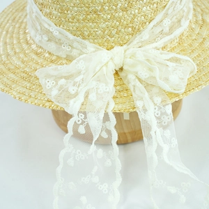 Close-up of a straw sun hat with elegant white floral lace embroidery and a bow detail