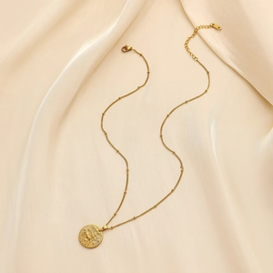 Close-up of gold stainless steel zodiac necklace on beige silk with K18 engraving detail