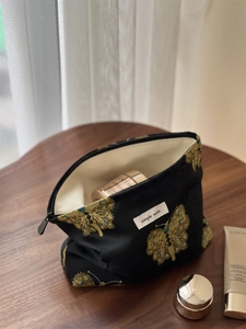 Detailed view of black satin makeup bag with golden butterfly embroidery and gem accents