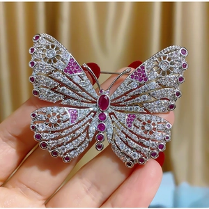 Elegante broche de mariposa en metal plateado calado con gemas rojas y cristales brillantes
