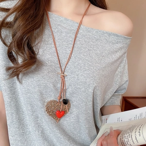 Detail of hollow heart pendant with red accent and brown leather cord necklace