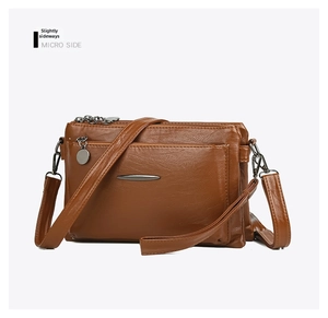 Detail of dark brown leather crossbody bag showing multi-zipper layers and pebbled texture