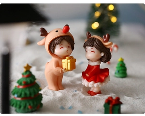 Close-up of cute Christmas couple figurines featuring a boy with a deer hat and gold gift box
