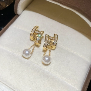 Macro detail of 14K gold plated H-shaped earrings with pavé zircon and hanging white pearls