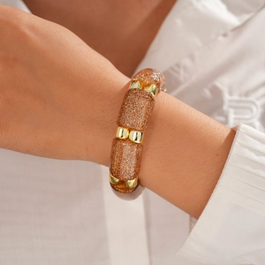 Detail of amber acrylic bracelet with gold glitter and polished metal beads on wrist