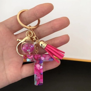 Close-up of pink resin letter T keychain with glitter star ball and golden tassel detail