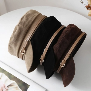 Primo piano di tre berretti newsboy vintage in kaki, nero e marrone con dettagli fibbia
