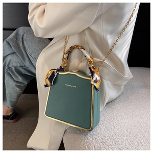 Detailed close-up of dark green textured leather box bag with silk scarf handle detail