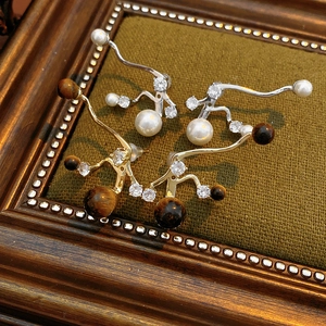 Makroaufnahme von Silber-Zirkon-Perlen und Gold-Tigerauge-Ohrringen in Vintage-Rahmen