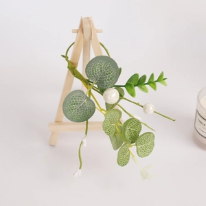 Green eucalyptus leaves and white pearl napkin ring hanging on a small wooden easel stand