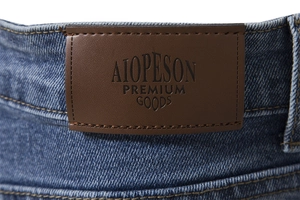 Detail of premium leather waist label on blue denim jeans showing embossed logo and texture