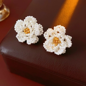 Macro shot of handcrafted white and gold seed bead flower earrings on a leather box