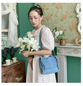 Close-up of a blue denim tote bag worn by a model in a vintage interior setting