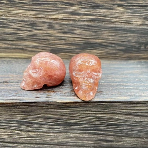 Hand-carved pink crystal skull figurines on natural wood surface, pair set