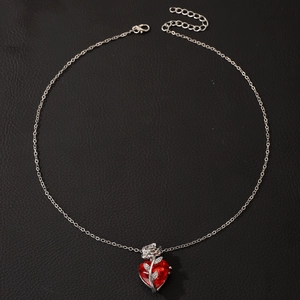 Detail of gothic silver necklace with red heart gemstone and winding rose pendant
