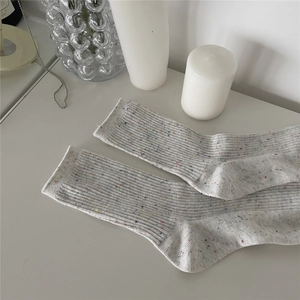 Close-up of light gray ribbed cotton socks with colorful specks in a minimalist setting