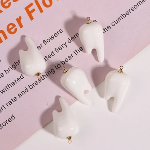Macro shot of five white 3D resin molar pendants with gold rings on pink background