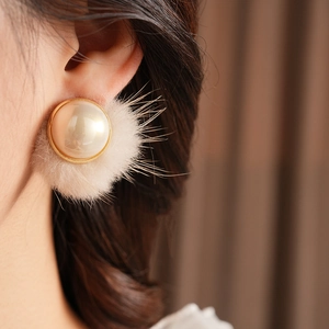 Close-up of elegant gold-rimmed pearl earring with cream plush faux fur detail