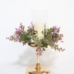 Detail of golden metal candle holder with glass shade and purple eucalyptus wreath