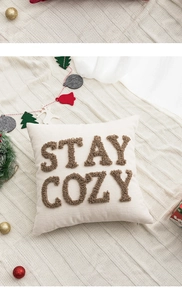 Detail showing Stay Cozy embroidery on a cream-white festive pillow with Christmas decor