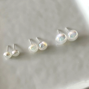 Detailed view of three pairs of iridescent white pearl studs in varying sizes on grey background