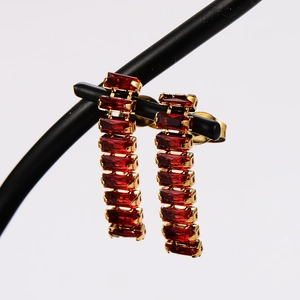 Detail of elegant gold earrings with long red rectangular stones on a black display stand