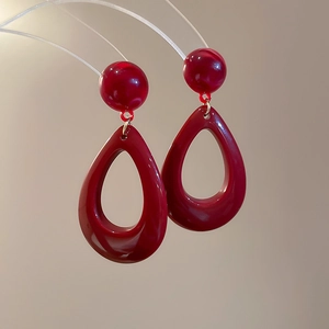 Close-up of elegant burgundy resin teardrop earrings hanging on a transparent stand