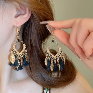 Detail of bohemian drop earrings with black tassels and gold leaf charms on hook