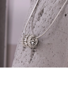 Macro shot of silver snake chain with crystal-encrusted cylinder pendant on rock