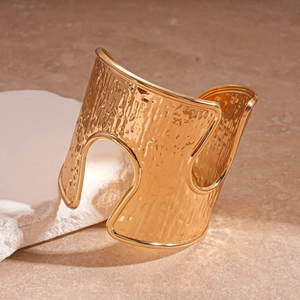 Detail of wide gold hammered bangle with asymmetric hollow cutouts on white stone