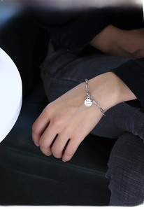 Macro shot of a minimalist silver link chain bracelet with round coin pendant on wrist