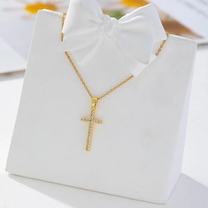 Detailed macro view of gold-plated cross necklace with pavé zircon stones on white stand