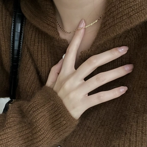 Close-up of a minimalist gold chain necklace worn over a cozy brown knitted sweater