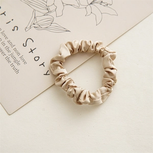 Detail shot of a champagne silk satin scrunchie with soft sheen and pleated texture